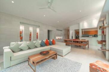 Spacious and modern living room with large sectional sofa, wooden coffee table, dining area, and open kitchen