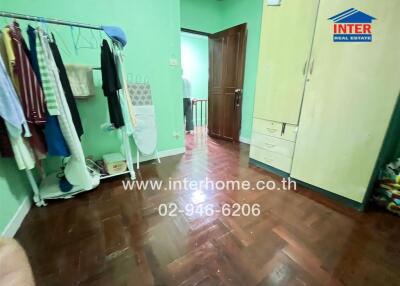 Bedroom with green walls, wooden floor, wardrobe, and clothes hanging on a rack