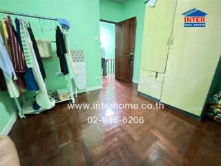 Bedroom with green walls, wooden floor, wardrobe, and clothes hanging on a rack