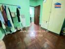 Bedroom with green walls, wooden floor, wardrobe, and clothes hanging on a rack