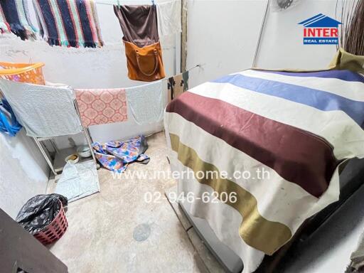 Simple bedroom with colorful bedding, clothes hanging, and a laundry basket