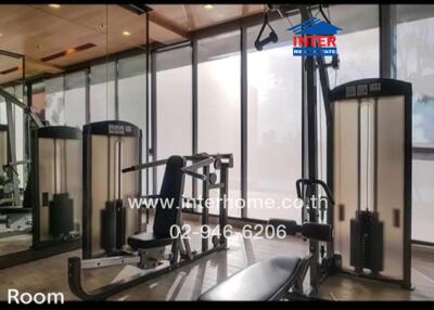 Fitness room featuring various exercise equipment including weight machines and benches, with large floor-to-ceiling windows.