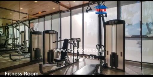 Fitness room featuring various exercise equipment including weight machines and benches, with large floor-to-ceiling windows.