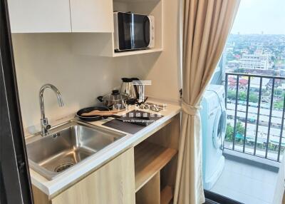 Compact kitchen area with sink, storage cabinets, microwave, and washing machine next to a balcony.