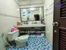 Bathroom with blue tile flooring, large mirror, and various toiletries