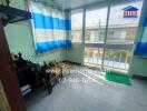 A modest balcony with tiled flooring, a transparent safety barrier, and colorful curtains with a view of neighboring buildings