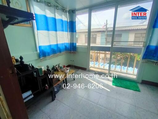 A modest balcony with tiled flooring, a transparent safety barrier, and colorful curtains with a view of neighboring buildings