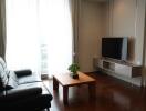 Modern living room with black leather sofa, wooden coffee table, and wall-mounted TV