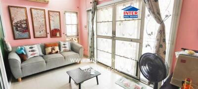 Living room with gray sofa, wall art, large windows, decorative curtains, and a fan