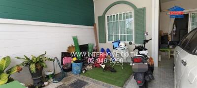 Photo of a garage area featuring a parked car, motorcycle, various gardening tools, and plants.