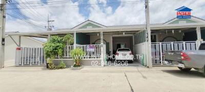 Exterior view of a single-story house with a gated driveway and garage, including a parked car and potted plants.