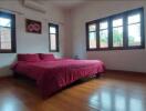 Bedroom with wooden floor, large windows, and red bedding