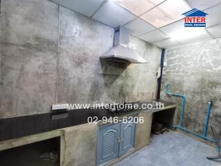 A kitchen with concrete walls, sink, and ventilation hood