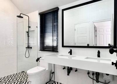 Modern bathroom with black and white geometric tile floor, dual sinks, large mirror, and walk-in shower