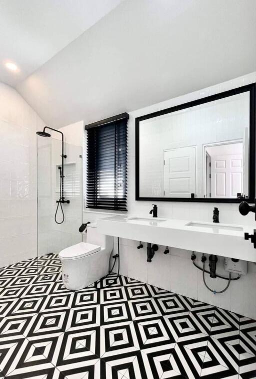 Modern bathroom with black and white geometric tile floor, dual sinks, large mirror, and walk-in shower