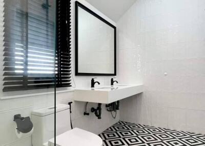 Modern bathroom with geometric black and white floor tiles, wall-mounted sink, and glass shower partition.