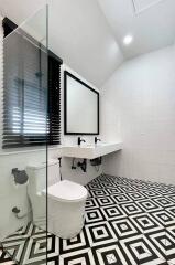 Modern bathroom with geometric black and white floor tiles, wall-mounted sink, and glass shower partition.