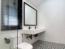 Modern bathroom with geometric black and white floor tiles, wall-mounted sink, and glass shower partition.