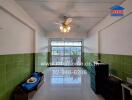 Interior view of a living area with green tiled walls, ceiling fan, and large windows.