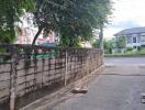 View of the street from the property with a concrete fence and trees in the background