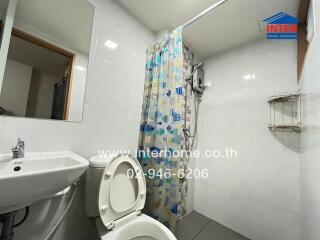 White-tiled bathroom with shower, toilet, and sink