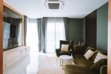 Modern living room with green couch, TV, and large windows