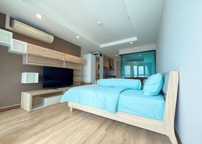 Modern bedroom with wooden flooring, a large bed, and entertainment area