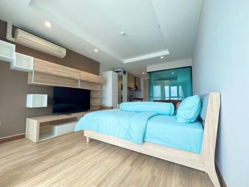 Modern bedroom with wooden flooring, a large bed, and entertainment area