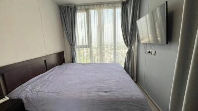 Bedroom with a large bed, mounted TV, and large windows with grey curtains