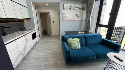 Modern living room and kitchen area in a property, with a blue sofa, wall art, and large windows.