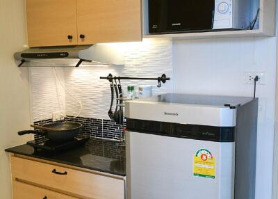 Compact kitchen with wooden cabinets, stainless steel fridge, microwave, and cooking area