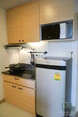 Compact kitchen with wooden cabinets, stainless steel fridge, microwave, and cooking area