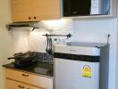 Compact kitchen with wooden cabinets, stainless steel fridge, microwave, and cooking area
