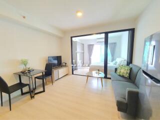 Well-lit living room with adjacent bedroom, featuring modern furniture and sleek design