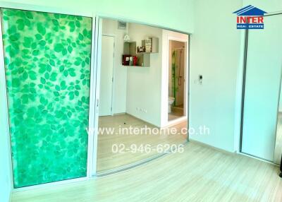 A spacious room with large green leaf-patterned sliding doors, light wooden flooring, and visible hallway leading to bathroom