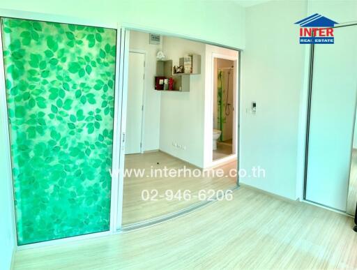 A spacious room with large green leaf-patterned sliding doors, light wooden flooring, and visible hallway leading to bathroom
