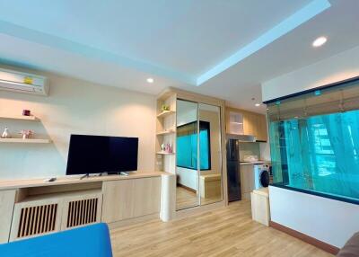 Modern living room with wooden flooring, built-in shelves, TV, and large glass window.