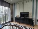 Modern living room with a TV, patterned rug, coffee table, and large window