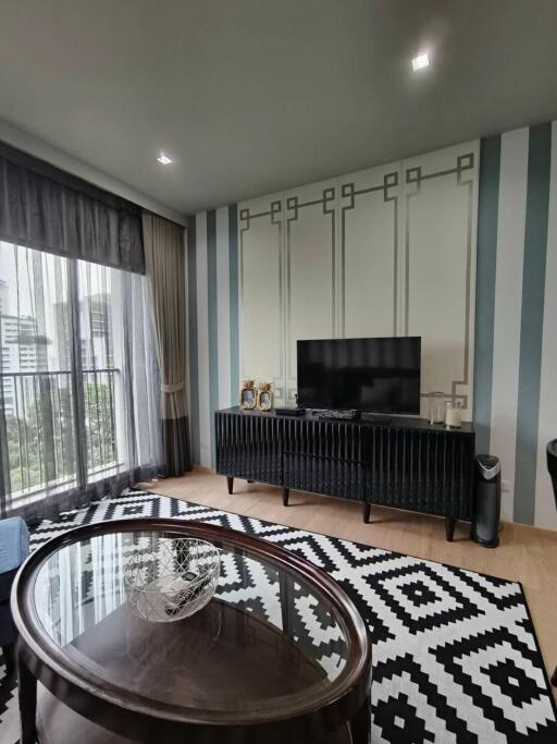 Modern living room with a TV, patterned rug, coffee table, and large window