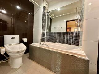 Modern bathroom with toilet, bathtub, and large mirror