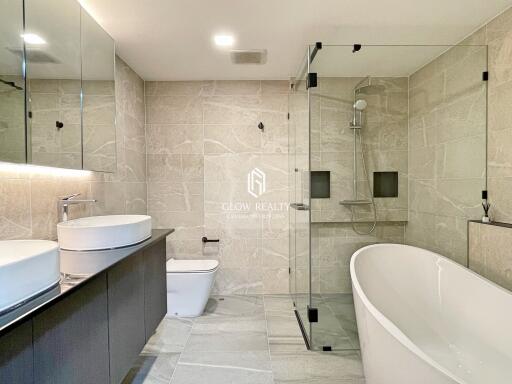 Modern bathroom with large glass shower, freestanding bathtub, vanity with two sinks, and toilet