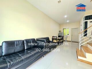 Living room with black leather sofas, dining table, and staircase