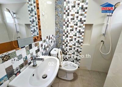 Bathroom with a sink, toilet, and shower area with decorative tiling