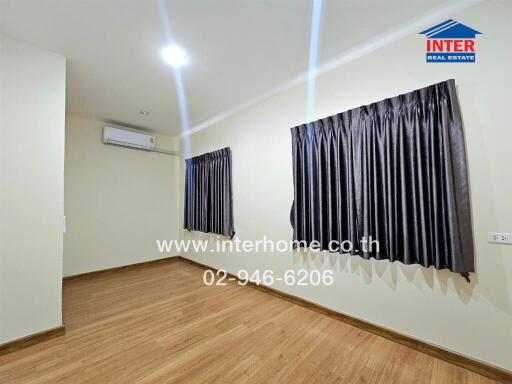 A minimalist bedroom with wooden flooring, split air conditioning, and large windows covered by dark curtains