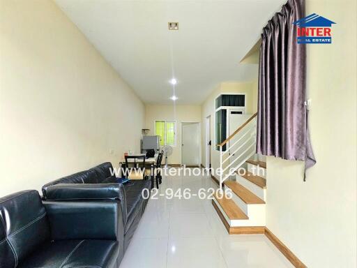 Living room with black sofa, dining area, staircase, and a website URL on the wall.