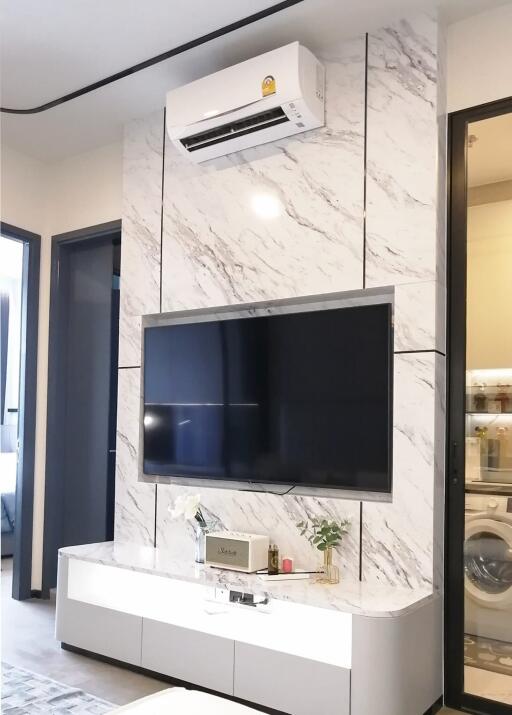 Living room with a TV mounted on a marble accent wall, air conditioner, and media console