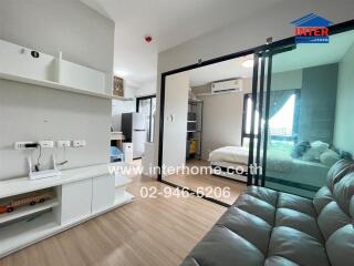 Modern living space featuring a small sitting area, a sliding glass door separating the bedroom, and a compact kitchen area.