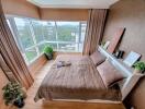 Well-lit bedroom with large windows, brown curtains, and potted plants