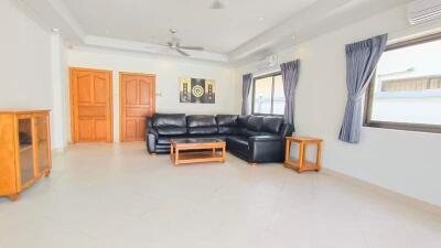 Spacious living room with a black leather sectional sofa, wooden furniture, large windows with blue curtains, and white walls.