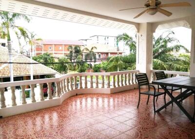 Spacious covered balcony with outdoor furniture and ceiling fan, overlooking a view with palm trees.